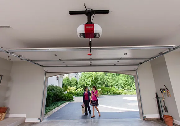 A wide view of a garage with an open door and a garage door opener installed, featuring two people walking outside.