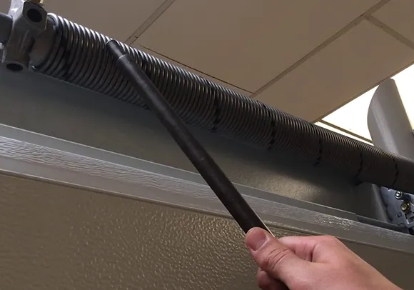 A hand adjusting a garage door torsion spring with a tool, illustrating precise torsion spring adjustment in Rocklin, CA.