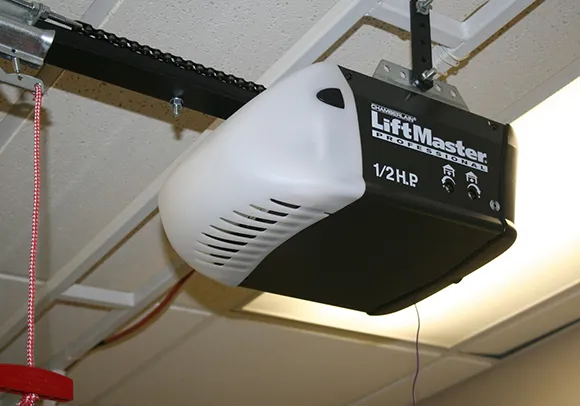 A close-up of a garage door opener mounted on the ceiling with a technician working on it.