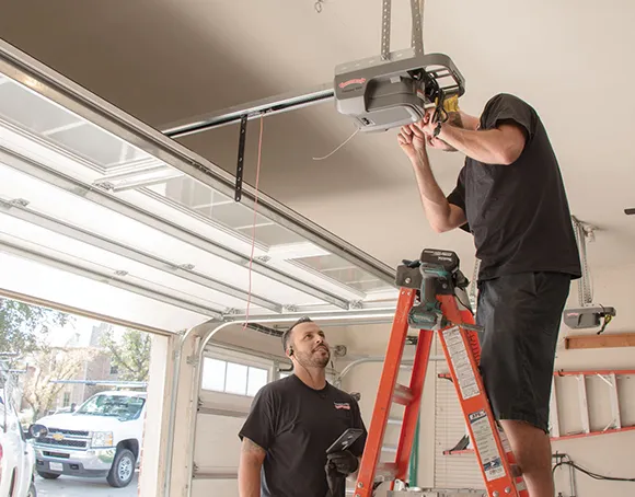 A technician installing a garage door opener on a ladder in a garage.