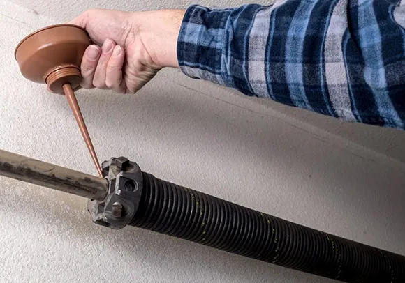 A hand holding a tool near a garage door torsion spring, showcasing trusted garage spring repair services in Elk Grove, CA.